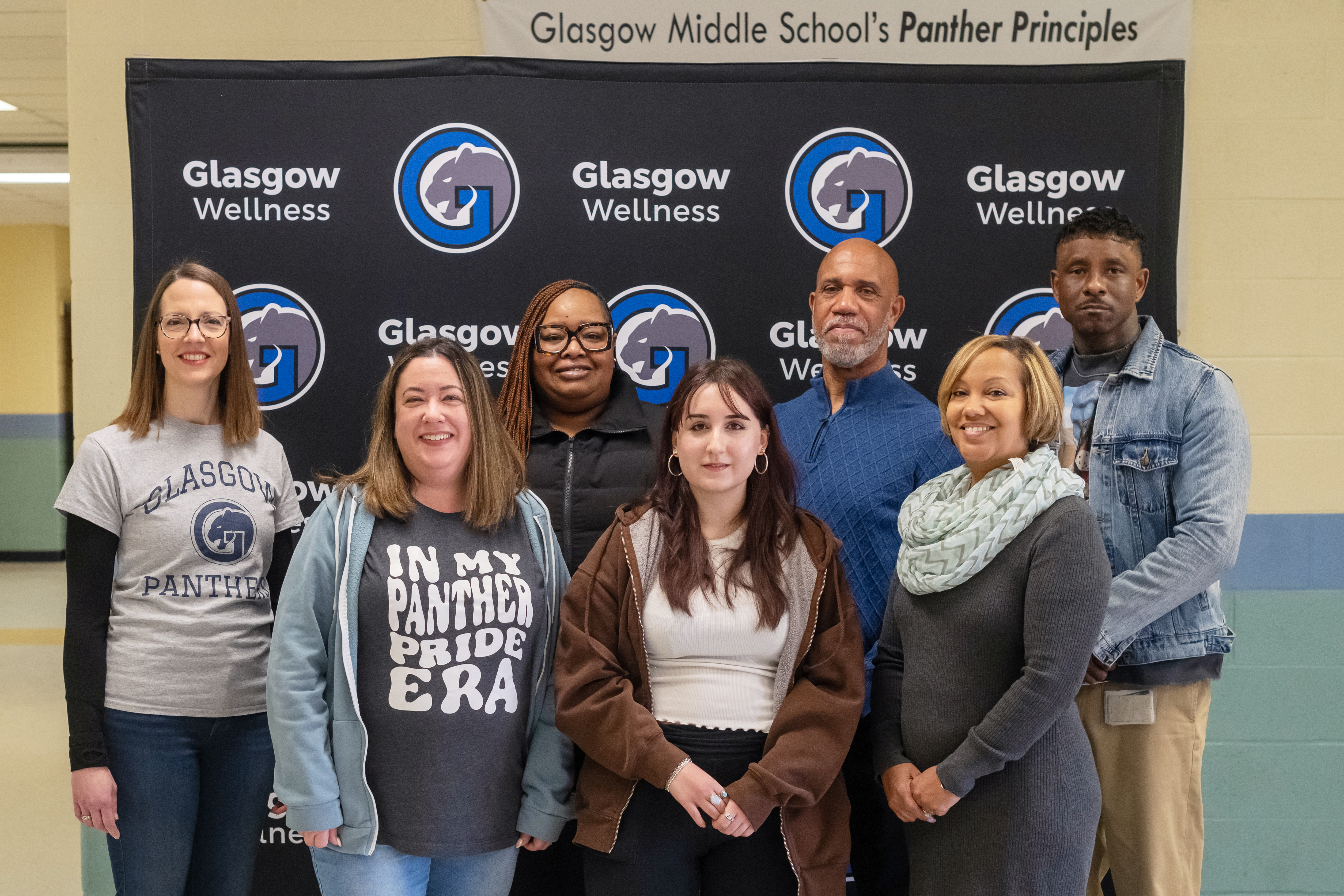 Seven adults pose for a group photo in front of a Glasgow Middle School backdrop.