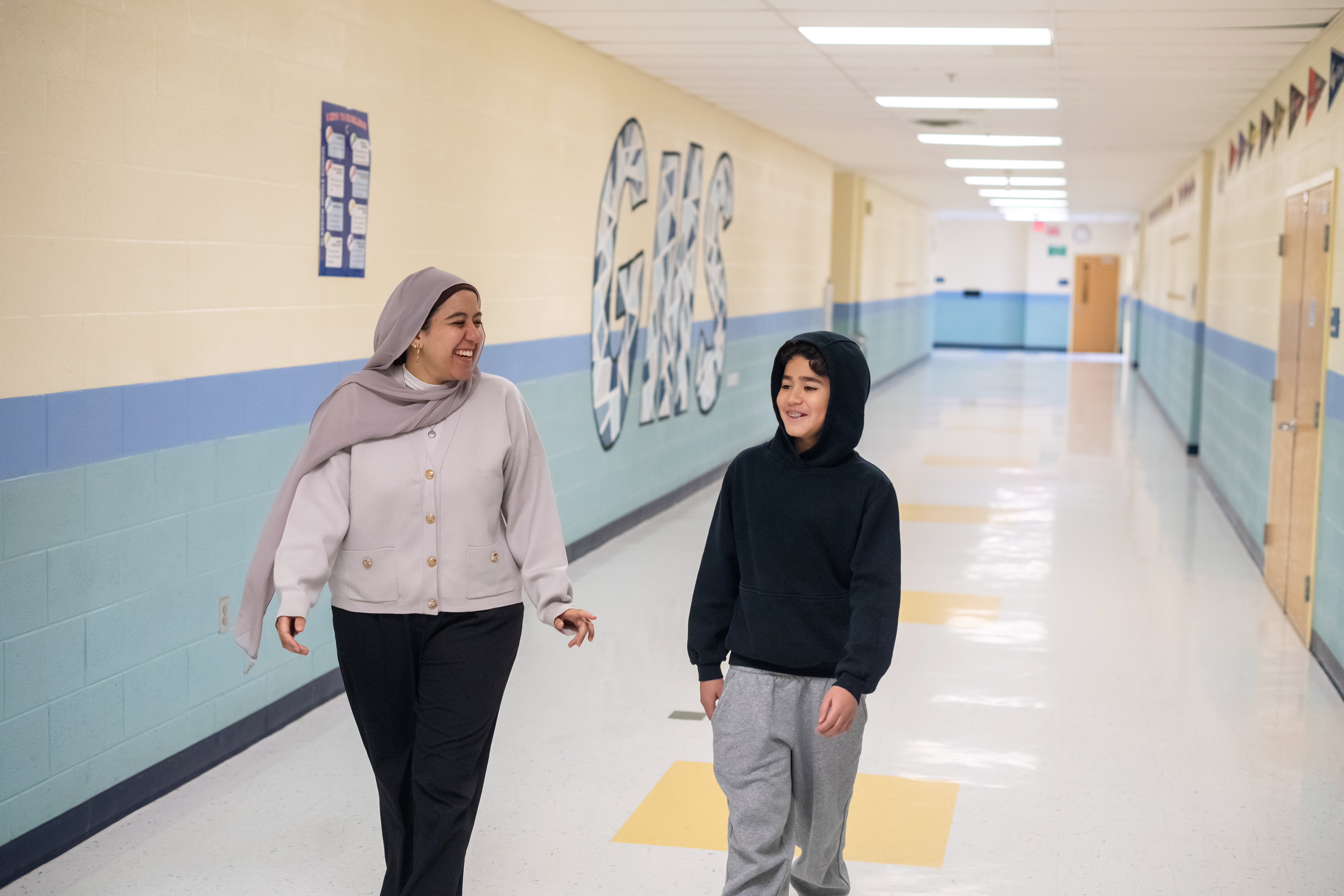 A woman, left, laughs as she walks down a hallway with a boy, right.